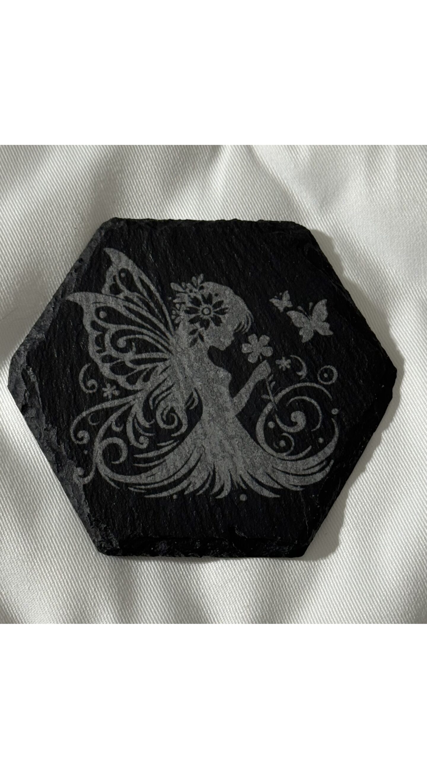 Black slate coasters featuring a delicate young fairies surrounded by flowers, one smelling blooms and one dancing with wings spread